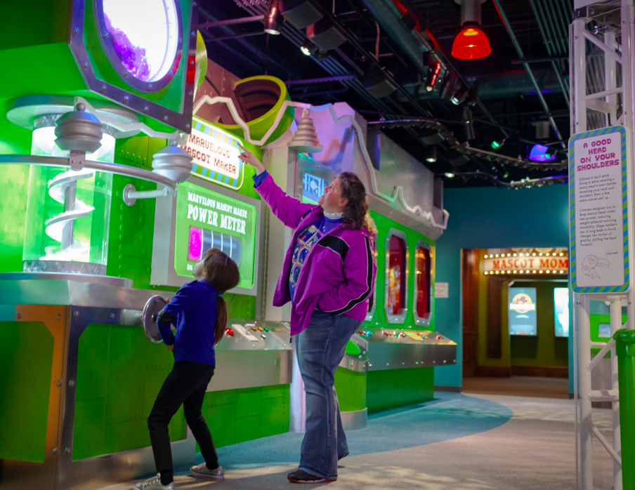 A woman and child investigate an interactive museum exhibit about mascots.