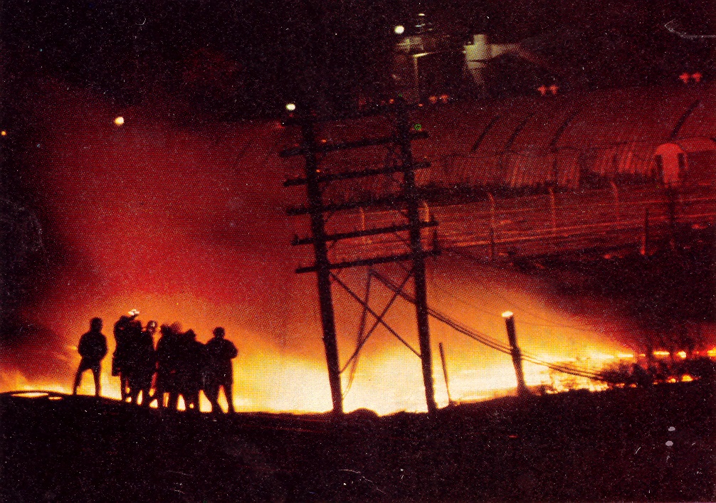 Silouettes of firefighters fighting fire with water illuminated only by fire in the night.